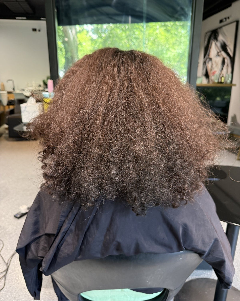 Thick, curly, frizzy shoulder-length hair seen from behind in the salon